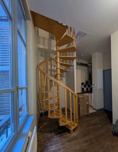 Escalier hélicoïdal bois encombrant, au cœur d’un espace de vie exigu, limitant les usages et la circulation.