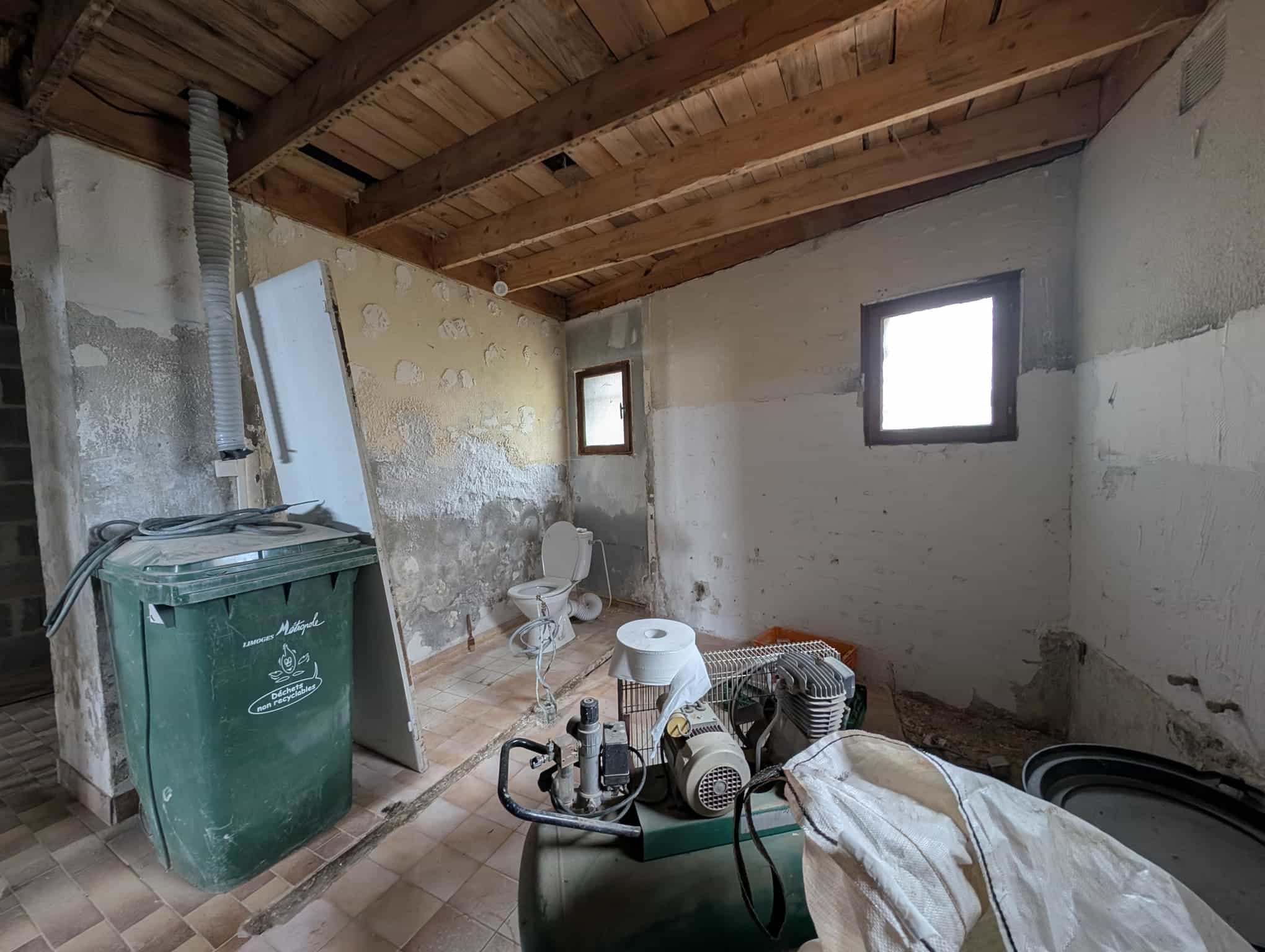 Pièce brute avec murs partiellement enduits et sanitaires démontés.