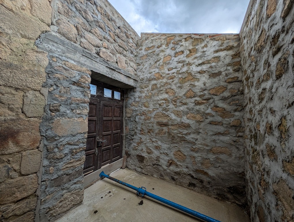 Vue intérieure de l'entrée avec ancienne porte en bois, murs en pierre, toiture en cours de réfection.