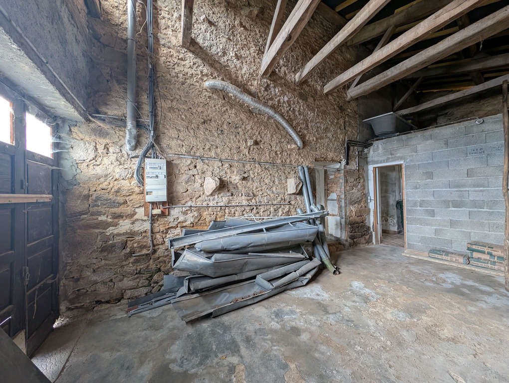 Vue du garage brut, mur en parpaings de la salle de bain et installations techniques apparentes.