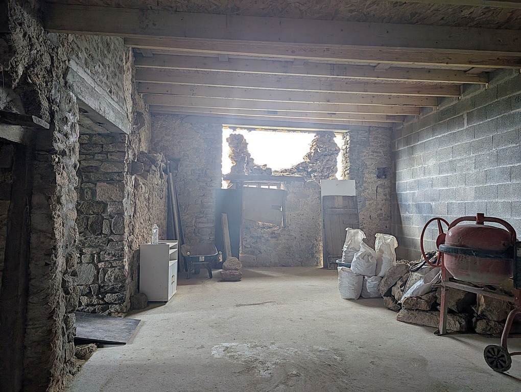 Vue de la grange pendant l'ouverture dans le mur, lumière pénétrant par une nouvelle baie, murs en pierre bruts.