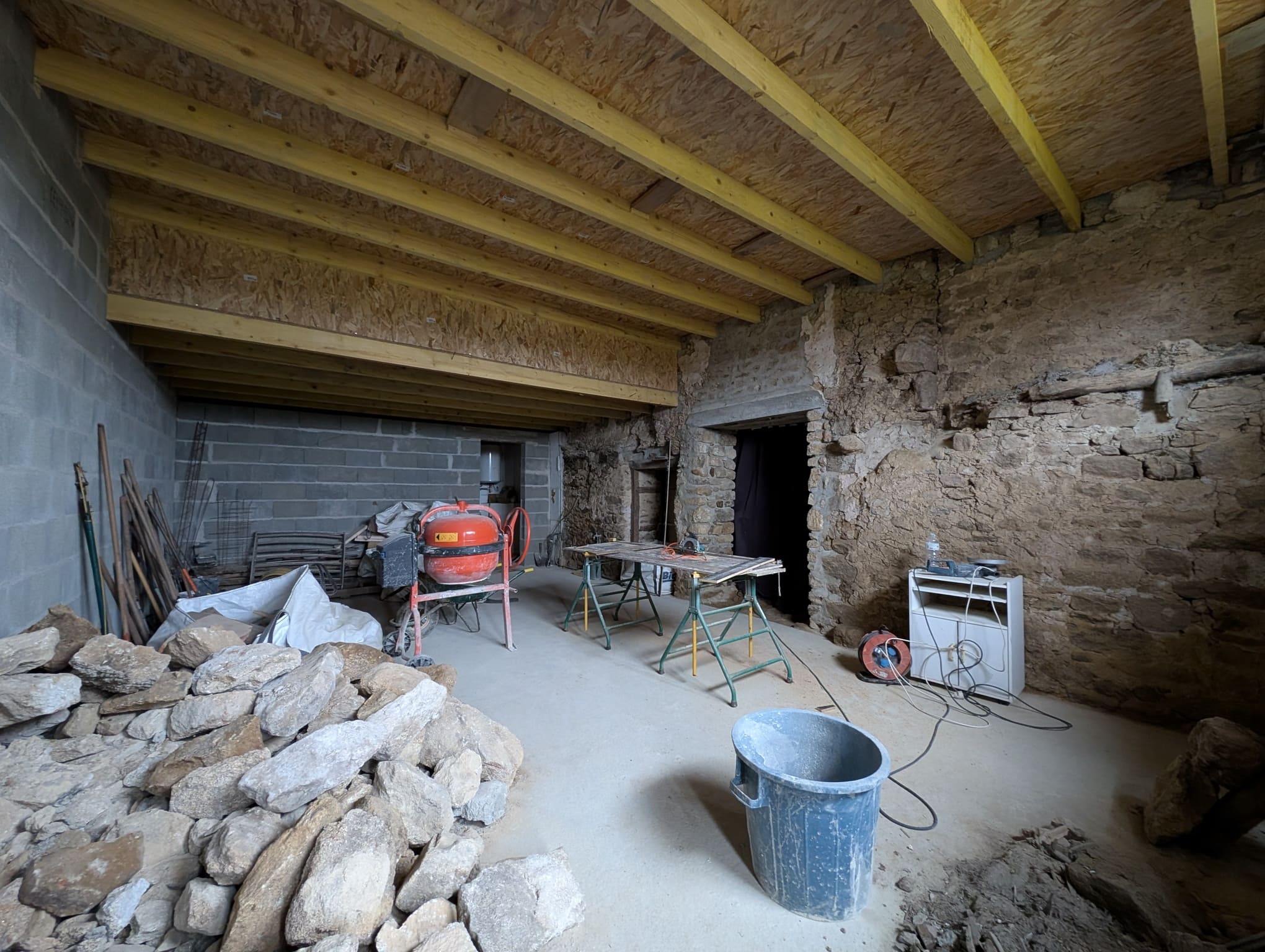 Intérieur de la grange en cours de transformation, murs en pierre, plafond en bois neuf.