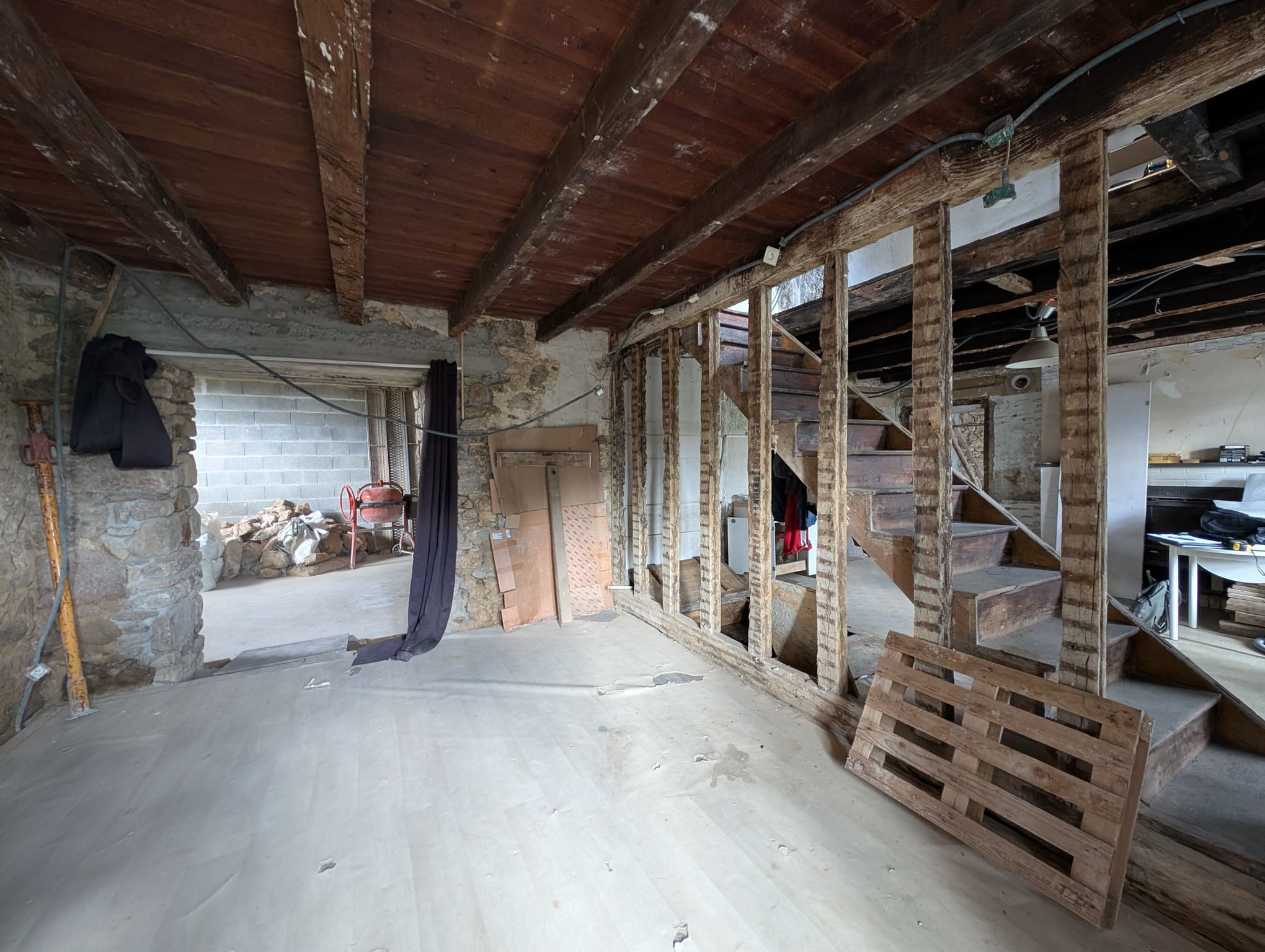 Intérieur après démolition, avec escalier en bois, cloisons démontées et ouverture vers volume annexe.