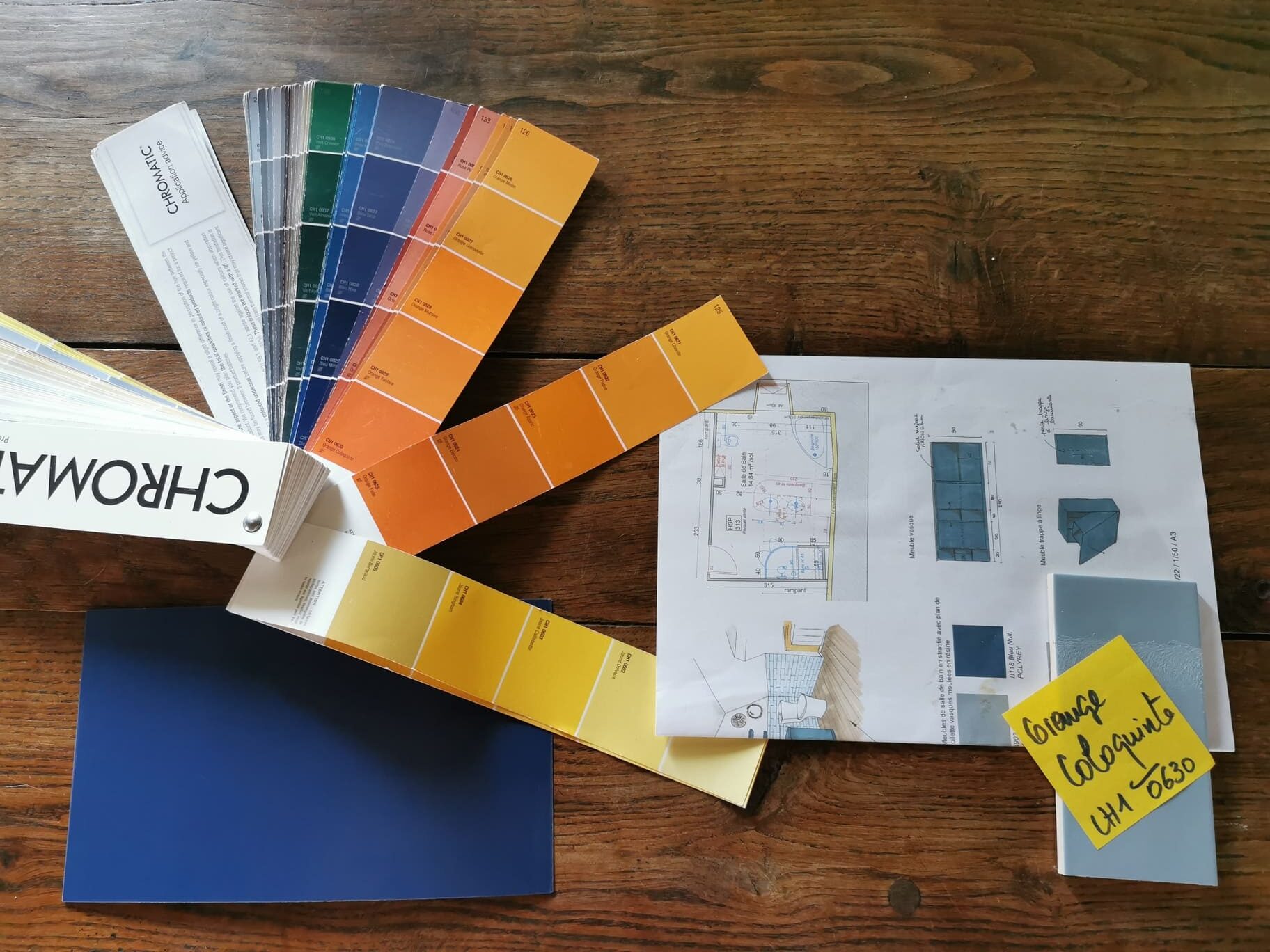 Photographie montrant le choix final des couleurs pour la salle de bain : nuancier déployé, échantillon de stratifié bleu nuit, faïence bleu clair et plan A3 du projet en arrière-plan.